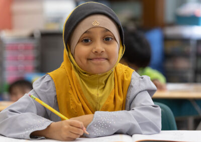 A girl with a hijab in a classroom, ready to write.